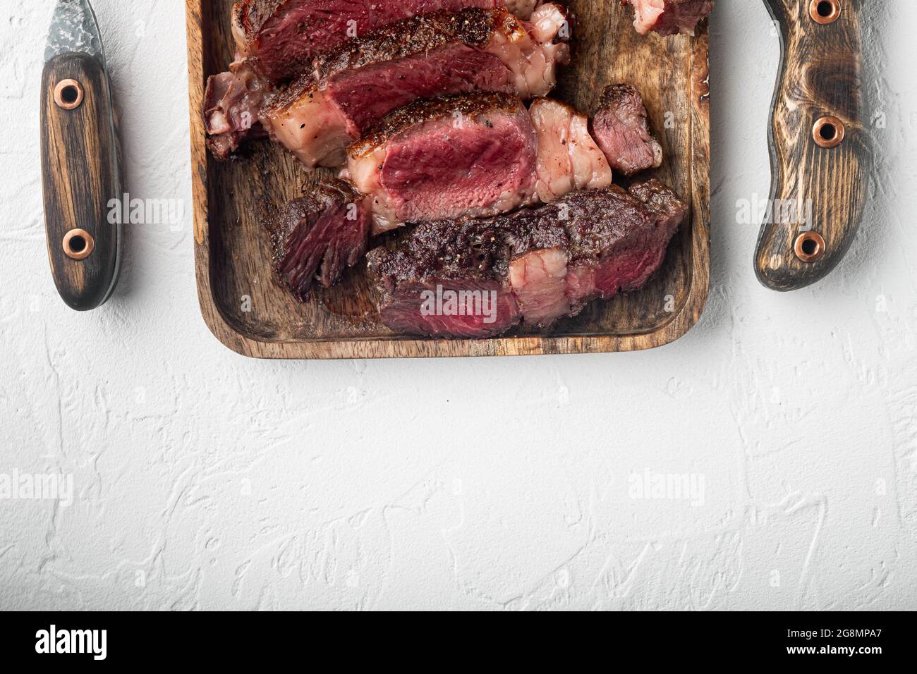 Barbecue dry aged Tomahawk Steak sliced medium rare set, on wooden serving board, on white stone background, top view flat lay, with copy space for te Stock Photo