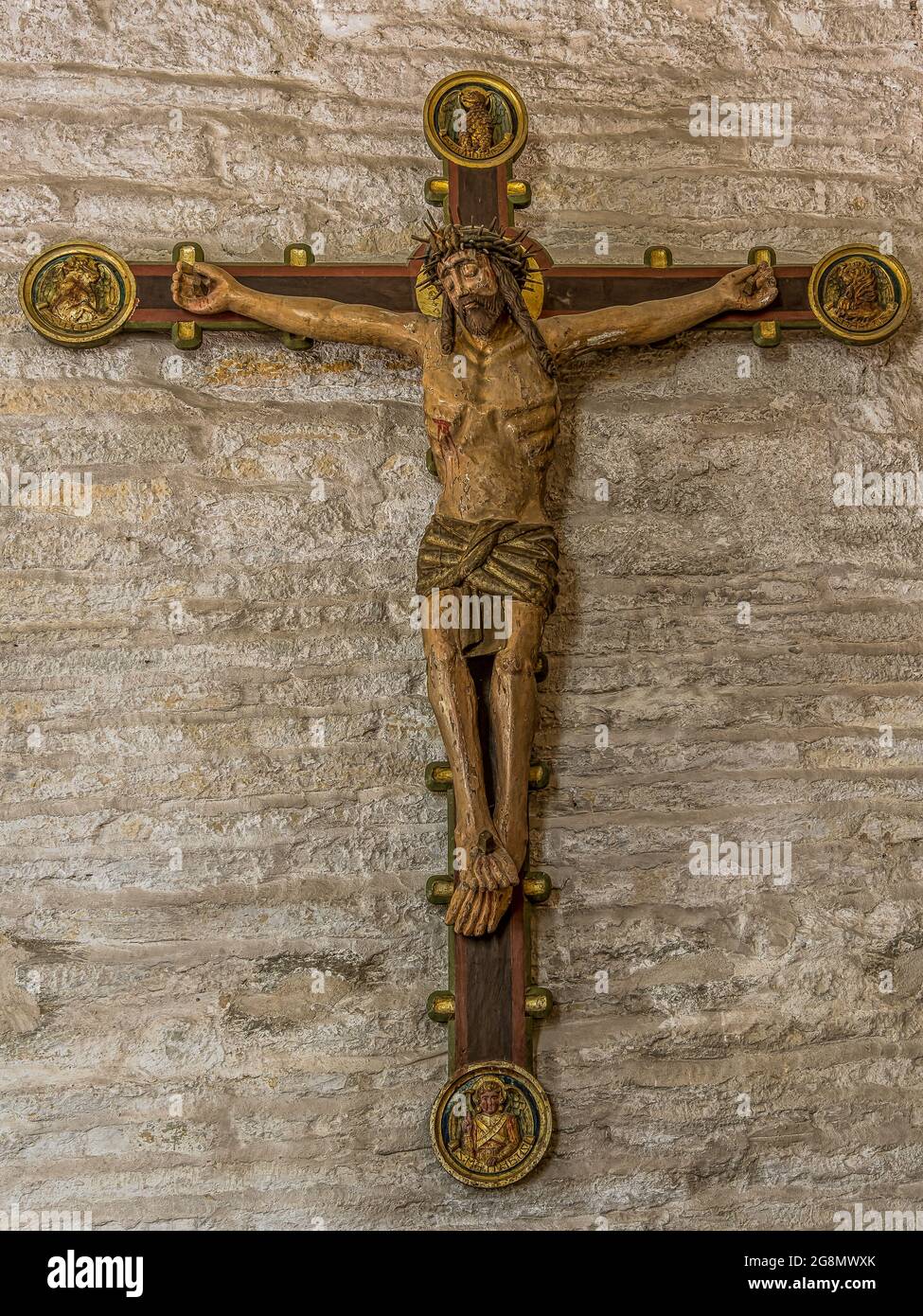 Jesus with the crown of thorns, an old colored crucifix from the 15th century with peeled painting haning on a stone wall in Borrie church, Sweden, Ju Stock Photo