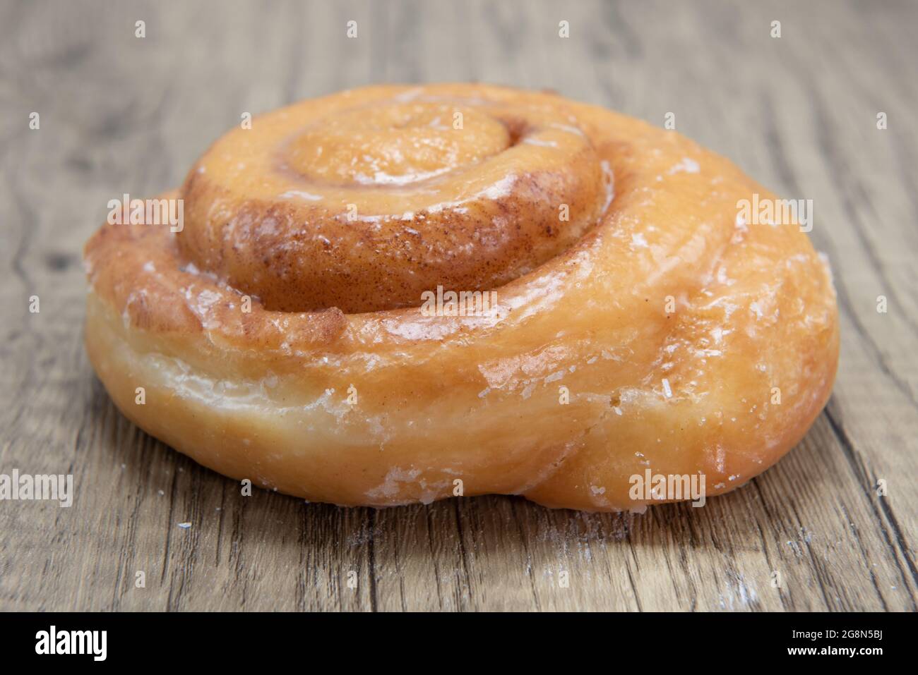 Cinnamon roll donut is textured with glazed coating for a sweet treat delight. Stock Photo