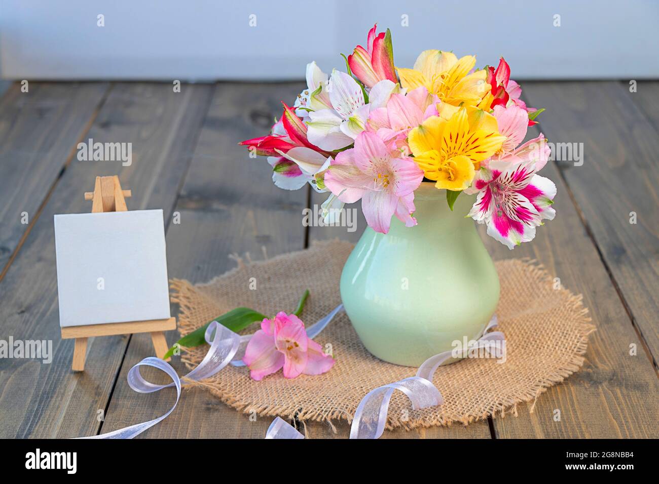 multi-colored flowers in a clay vase, empty molbert with copy space on a wooden background. multicolored alstroemeria, pink, yellow, magenta, white an Stock Photo