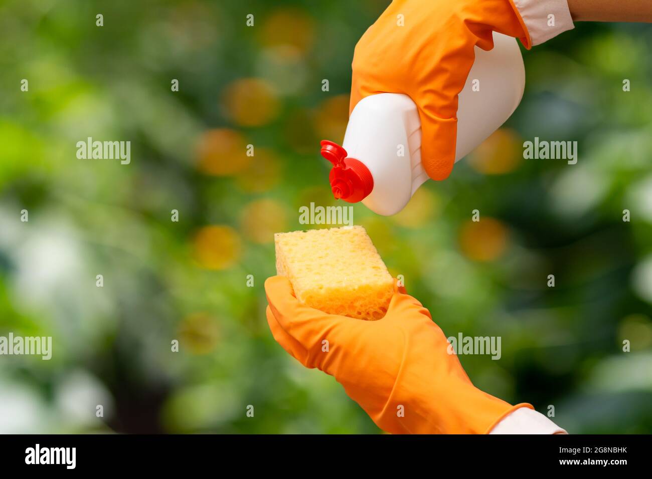 Woman's hands in orange protective gloves with a bottle of dishwashing ...