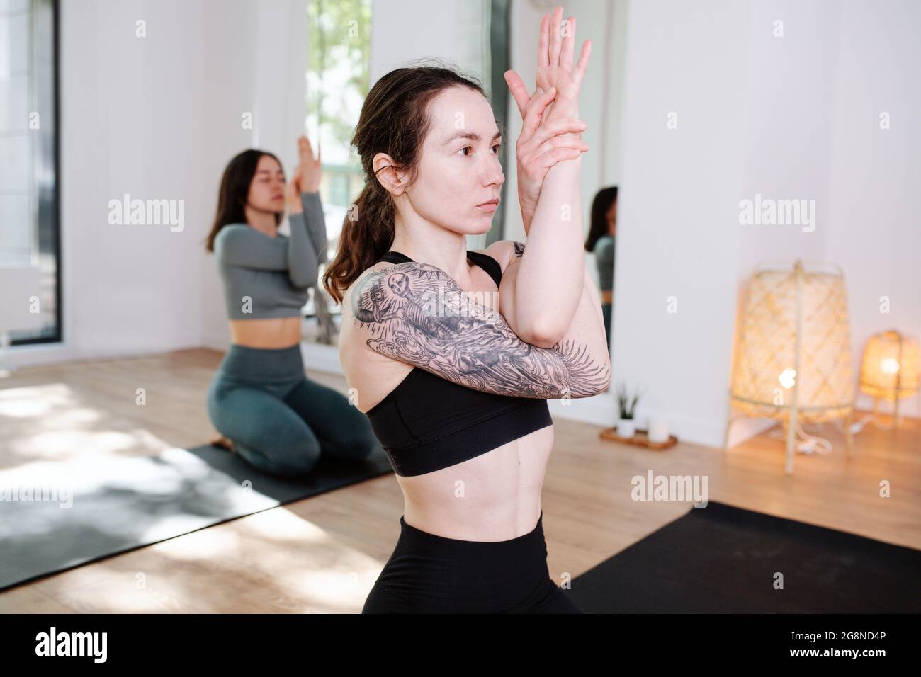 Conentrated women in sportswear practicing yoga in a group, meditating with  arms interlaced in a big studio. Focus on a girl with big shoulder tattoo  Stock Photo - Alamy