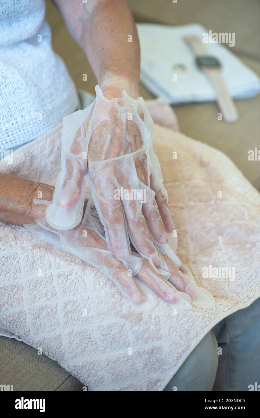 Senior woman wearing hand mask gloves. Moisturizing gloves to soften and protect hand skin. Hands close up. Stock Photo