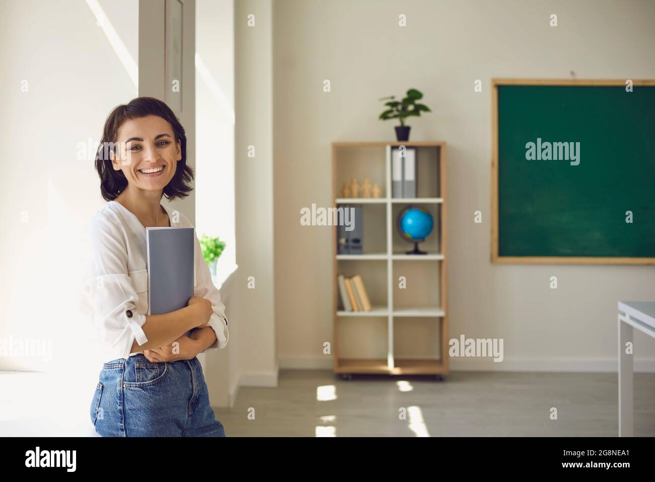 A beautiful smiling girl student stands sideways at the window Stock Photo