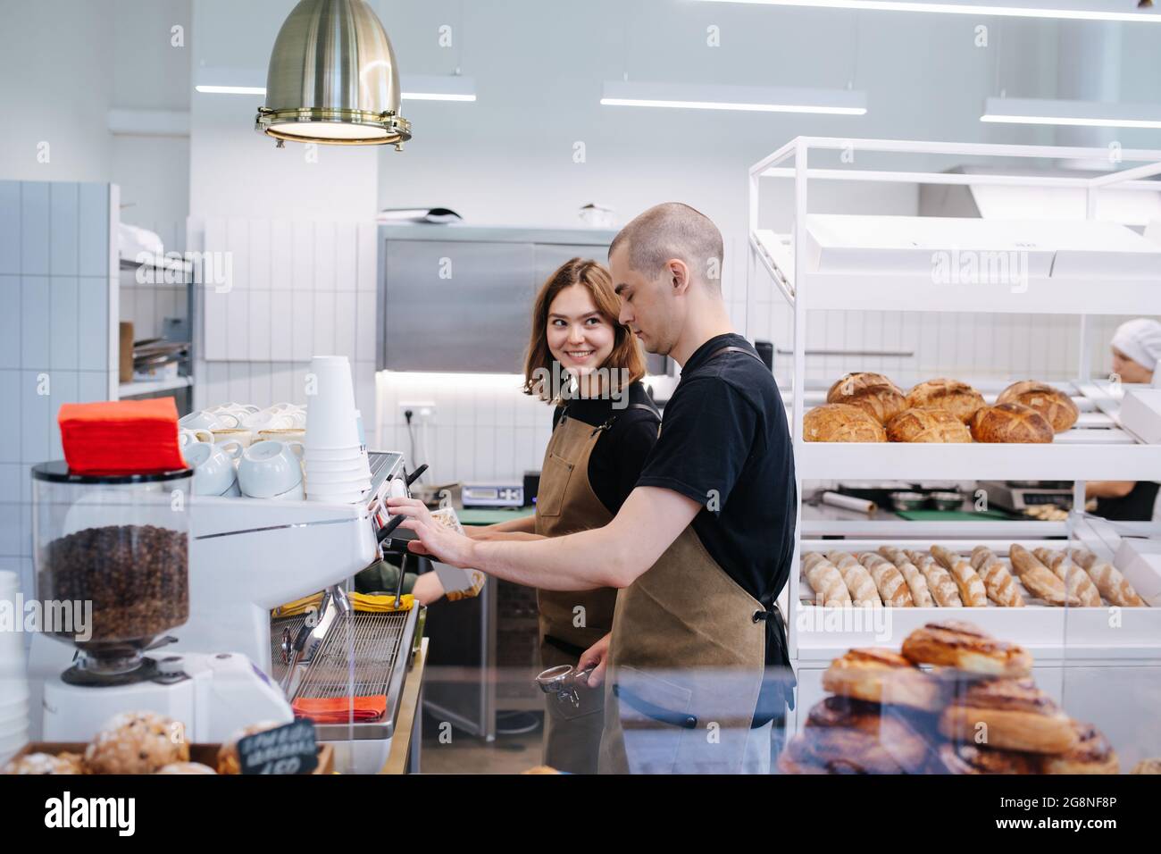 Coworkers, young man and woman socialising in the bakery kitchen. Side view. She's smiling at him. Stock Photo