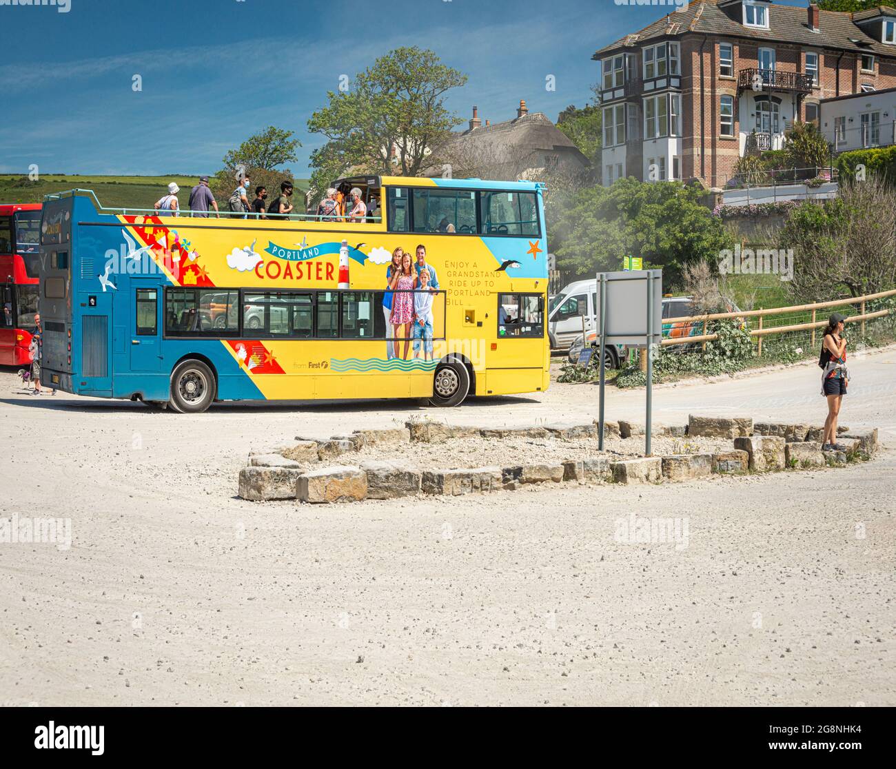 Jurassic Coaster open top bus with tourists embarking off in Lulworth Cove dusty car park with blue sky and a hot summer's day. West Lulworth, Wareham. Stock Photo
