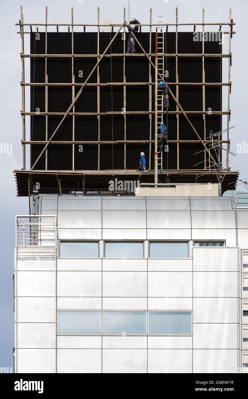 Workmen moving around scaffolding on an advertising board atop a building in Roppongi, Tokyo, Japan. Friday March 26th 2021 Stock Photo
