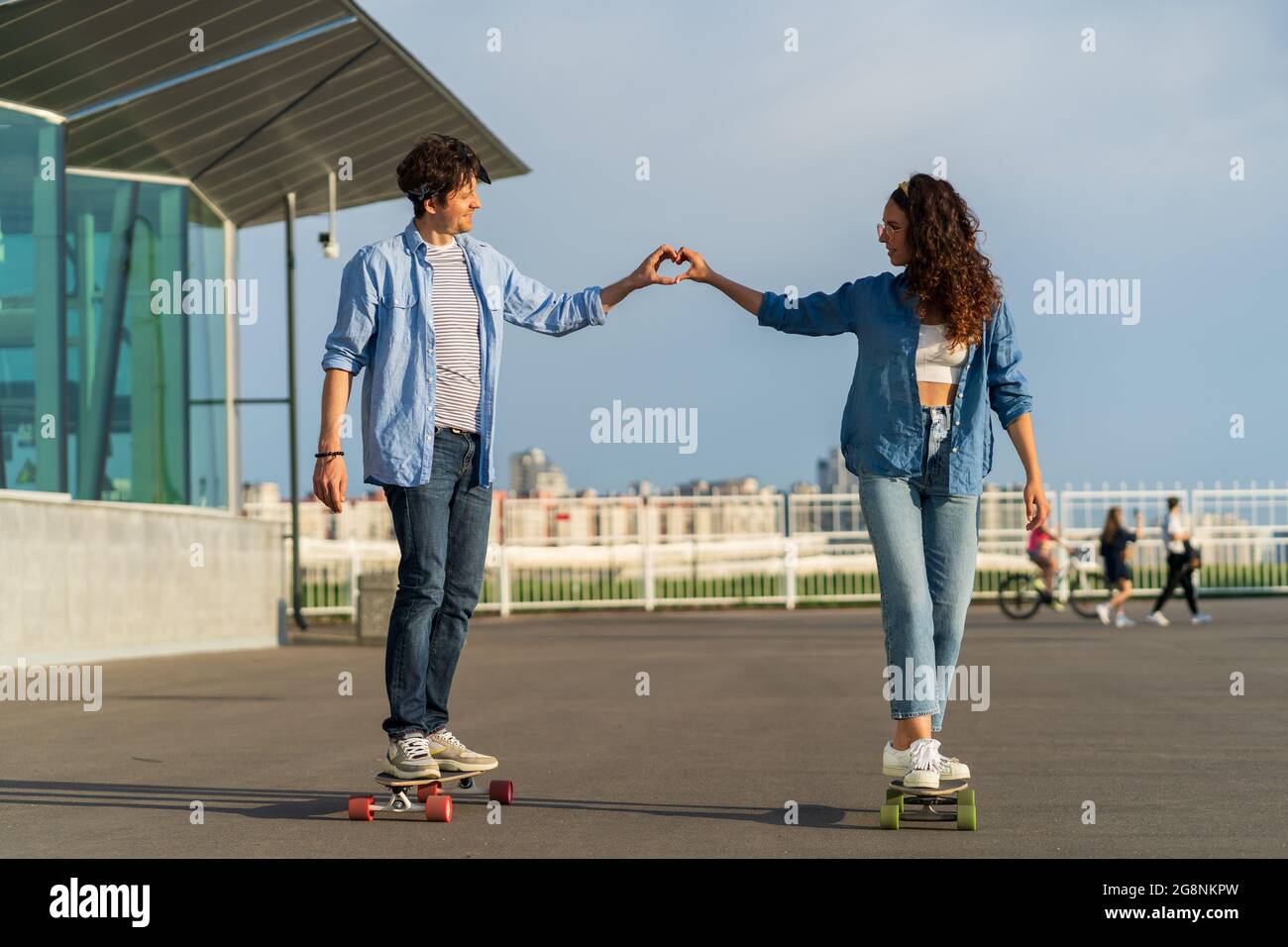 Romantic man and woman ride longboard show heart shape. Trendy couple in love outdoors enjoy date Stock Photo