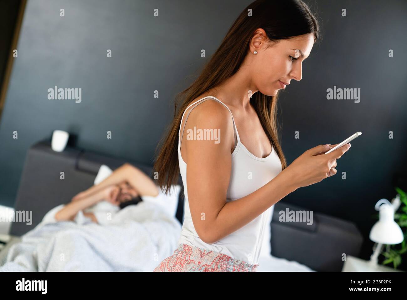Woman talking privately on cellphone while her husband sleeping on bed Stock Photo