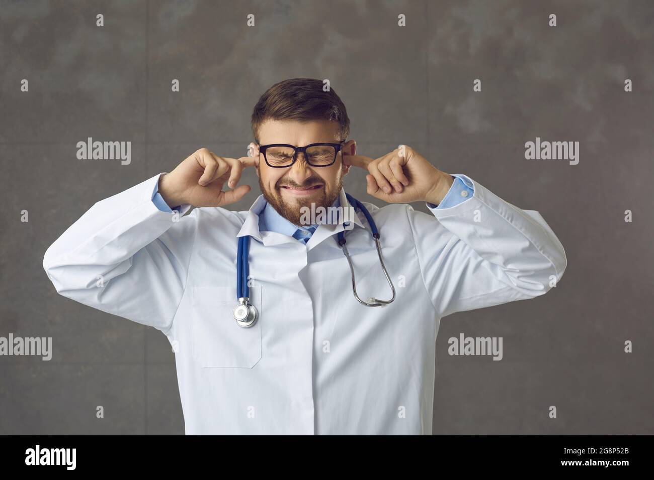 Annoyed stressed doctor closes ears with fingers trying to ignore loud hospital noises Stock Photo