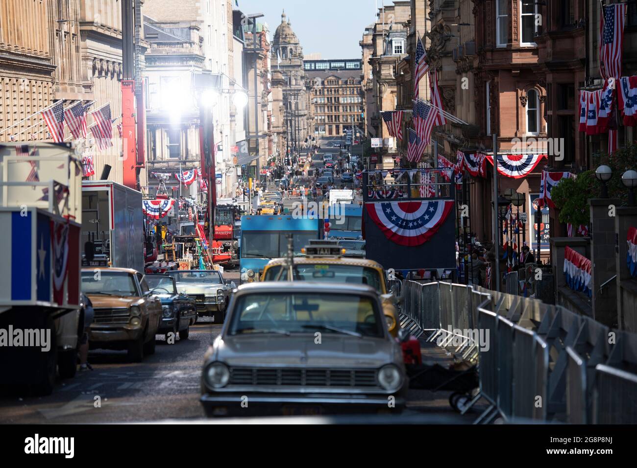 Glasgow, Scotland, UK. 21 July 2021.  PICTURED: A view down St Vincent street showing parked 1950/60s cars on the film set with a gantry of extremely bright set lights. Filming on the set of Indiana Jones 5 in the middle of Glasgow city centre as the Hollywood blockbuster sets up Glasgow as New York City. A full production can be seen, with a large cast, producers and extras. The city centre has been changed so that all the shop fronts and building look like 1959 America. Credit: Colin Fisher Stock Photo