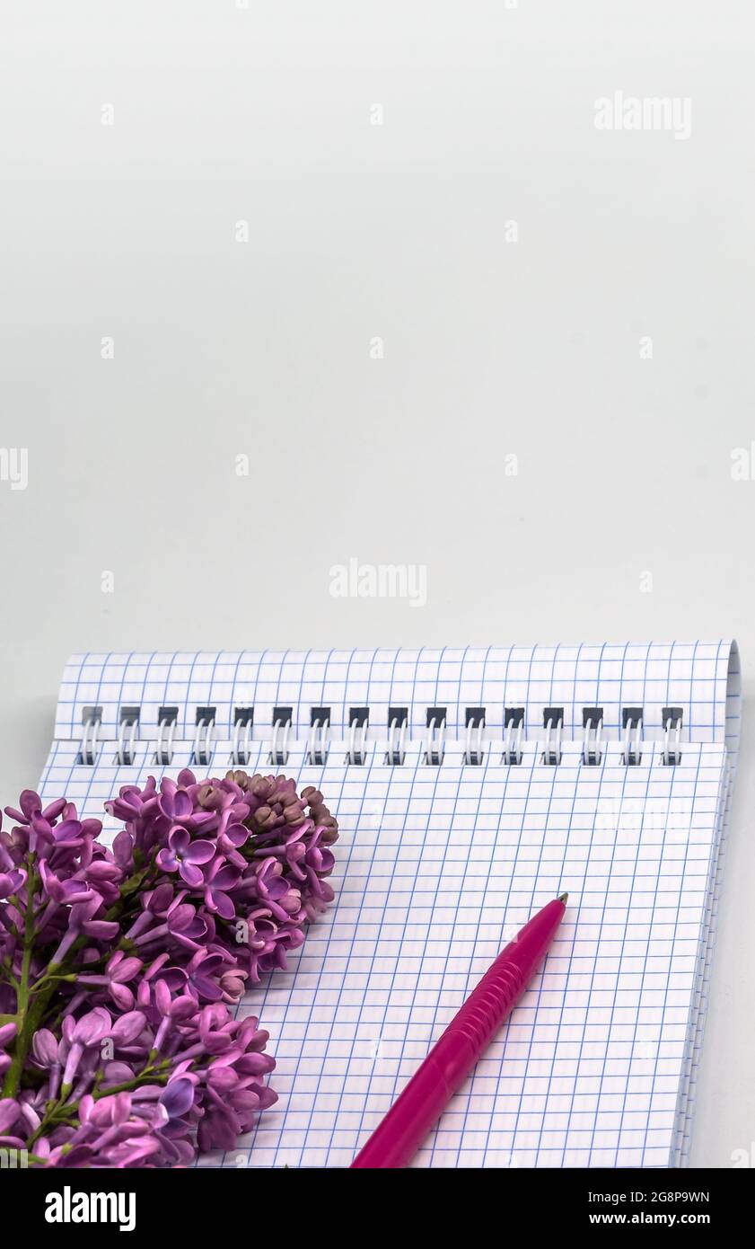 Notebook lilacs on white background. Spiral notebook and pen. Notepad with pen and flowers. Stock Photo