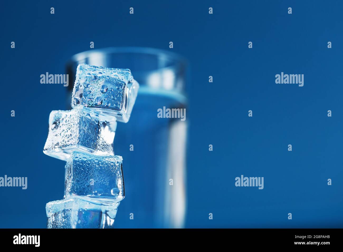 A glass of refreshing water and a tower of ice cubes on a blue ...