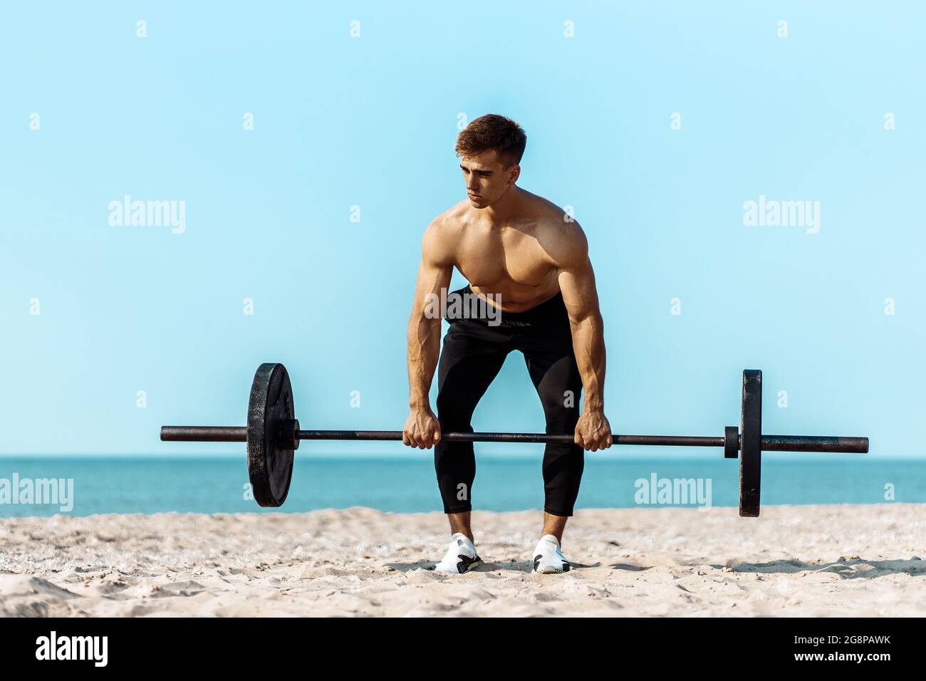 Healthy handsome active man with fit muscular body, young muscular man lifting weights, doing exercises, Sporty man exercising on the beach, Outdoor t Stock Photo
