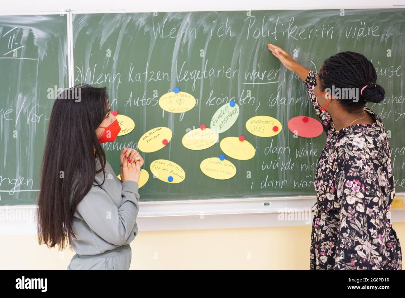 Berlin, Germany. 22nd July, 2021. Student Tasneen Al Sahli (l) and teacher Nicha Wahlstab stand at the blackboard in a summer school at the Oberstufenzentrum (OSZ) Bekleidung und Mode in Kochstraße. As part of the 'Stark trotz Corona' catch-up program, the Senate Department for Education is offering a summer school again this holiday season. Credit: Jörg Carstensen/dpa/Alamy Live News Stock Photo