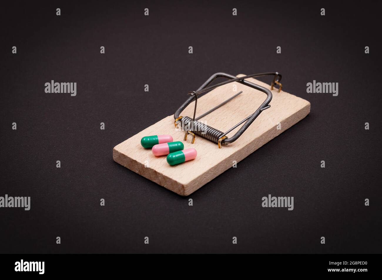 Pharmaceutical Addiction or Big Pharma Trap - Colored Pills or Capsules in Wooden Mousetrap on Black Background Stock Photo