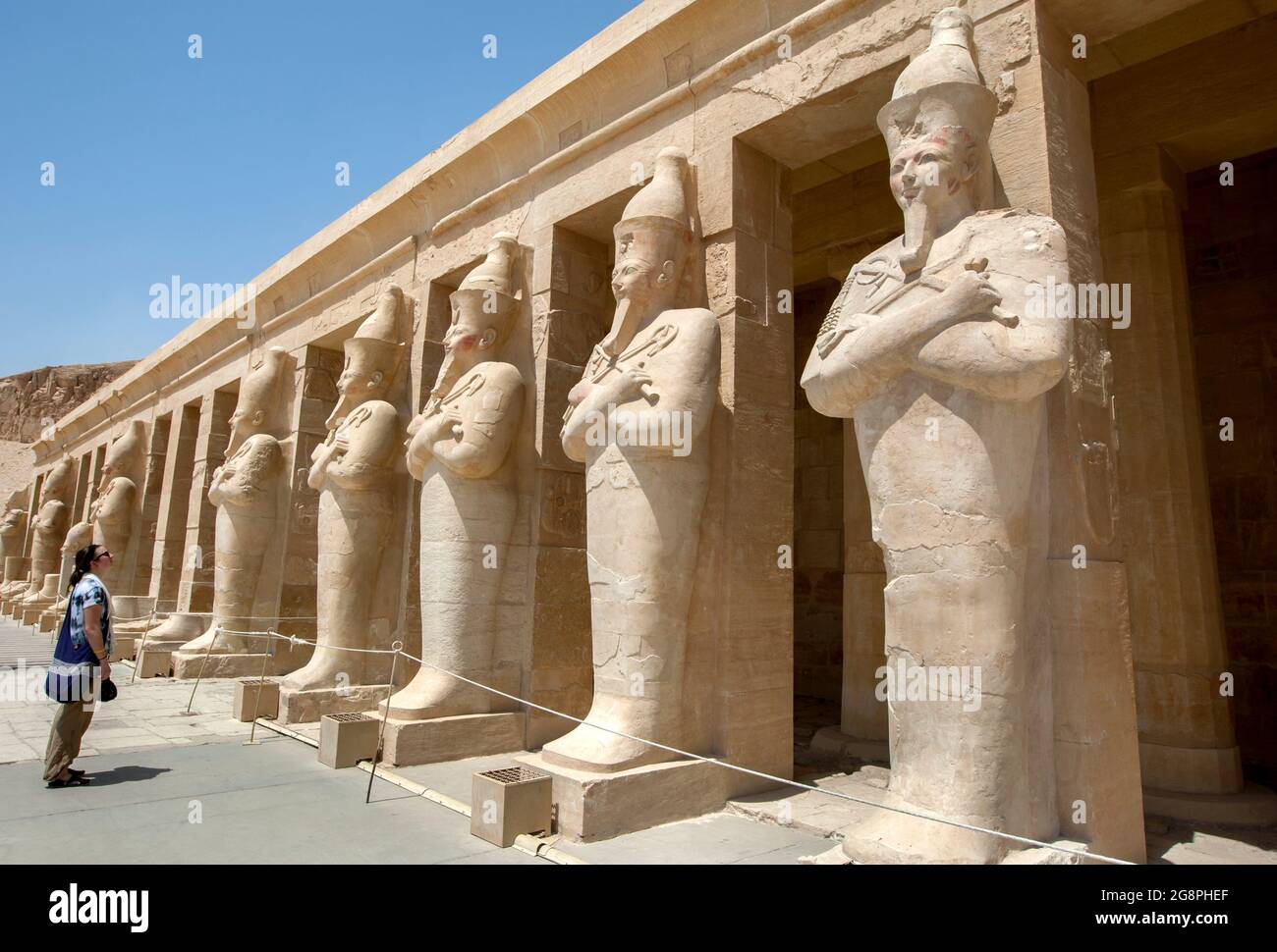 A tourist admires the row of Osiris pillars which stand along the upper terrace at the Mortuary Temple of Hatshepsut at Stock Photo