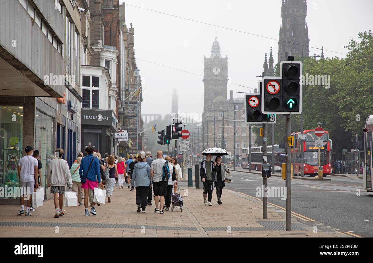 Princes Street, Edinburgh, Scotland, UK weather. 22nd July 2021. Dull  and dreary weather in Scottish capital, the overnight haar taking its time to clear from the higher viewpoints such as the Castle, Calton Hill and Arthur's Seat.Temperature 21 degrees centigrade. Pictured: shoppers and people on Princes Street with a misty Calton Hill in background. Credit: Arch White/Alamy Live News Stock Photo