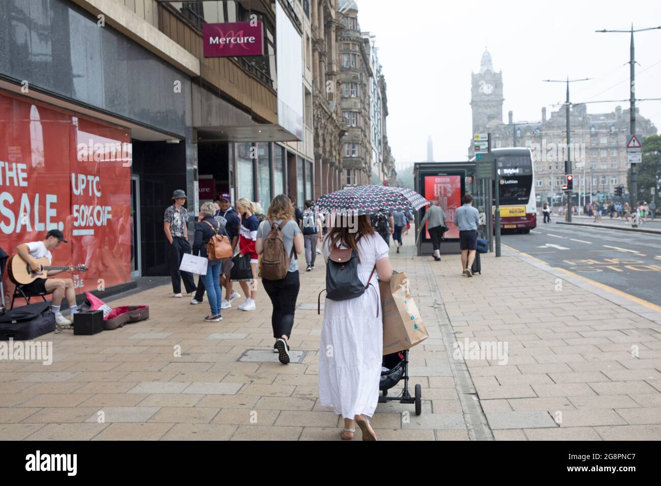 Princes Street, Edinburgh, Scotland, UK weather. 22nd July 2021. Dull  and dreary weather in Scottish capital, the overnight haar taking its time to clear from the higher viewpoints such as the Castle, Calton Hill and Arthur's Seat.Temperature 21 degrees centigrade. Pictured: shoppers and people on Princes Street with a misty Calton Hill in background. Credit: Arch White/Alamy Live News Stock Photo