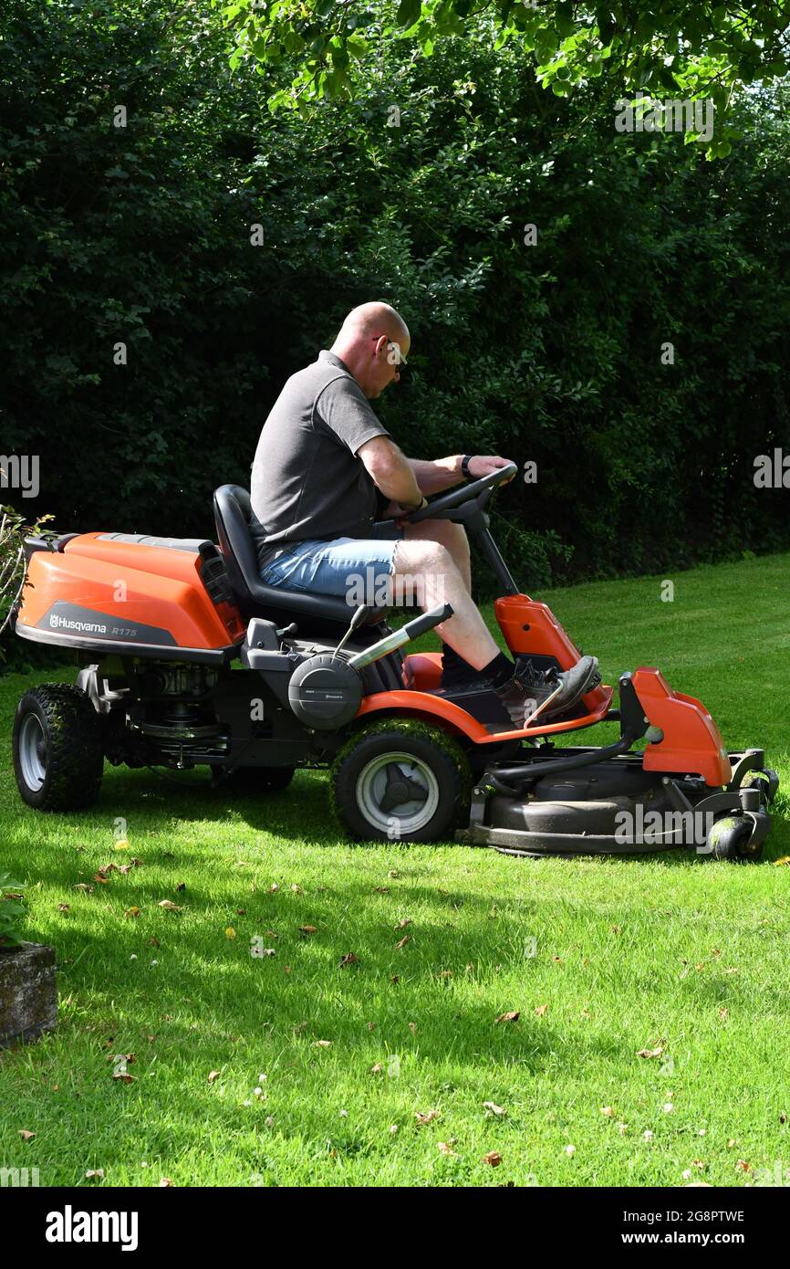 A male on a drive on lawn mower cutting the grass on a summers day Stock Photo