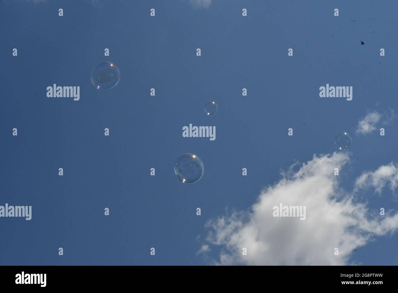 Four bubbles floating against a light blue sky with passing clouds Stock Photo