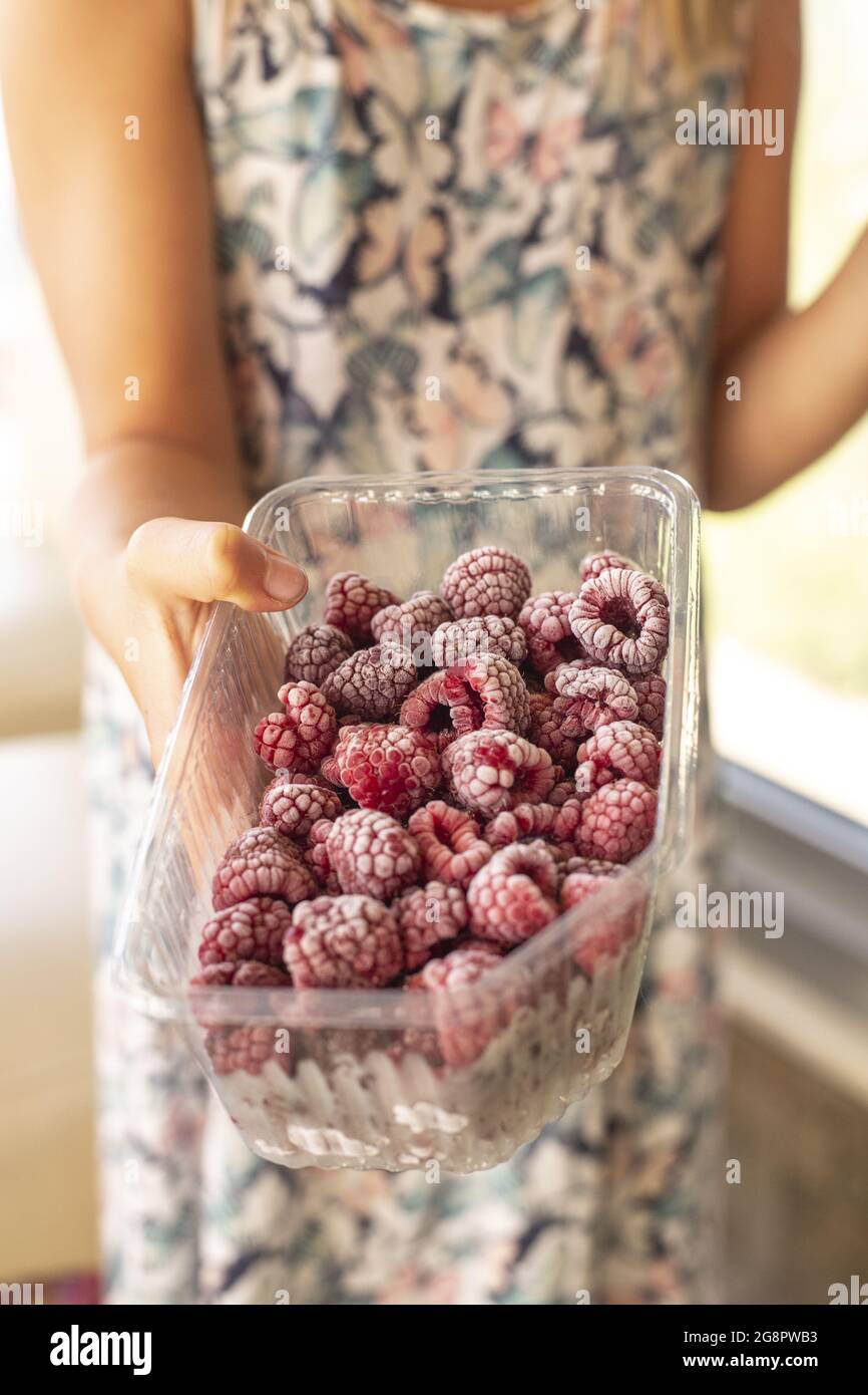 Vertical shot of a woman holding a plastic container filled with frozen ...