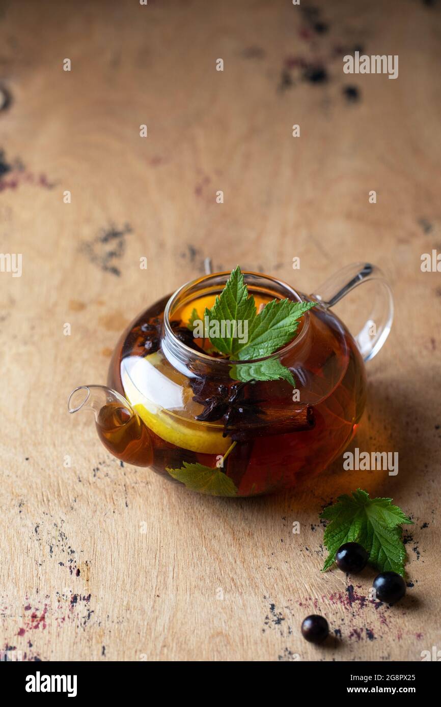 A teapot with black tea with currant berries, lemon, a cinnamon stick. Autumn background. Copy space. Stock Photo