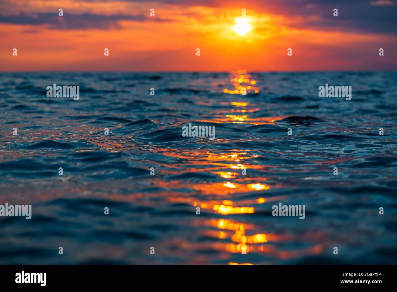 Sunset with clouds, warm colors and waves in ocean. Stock Photo