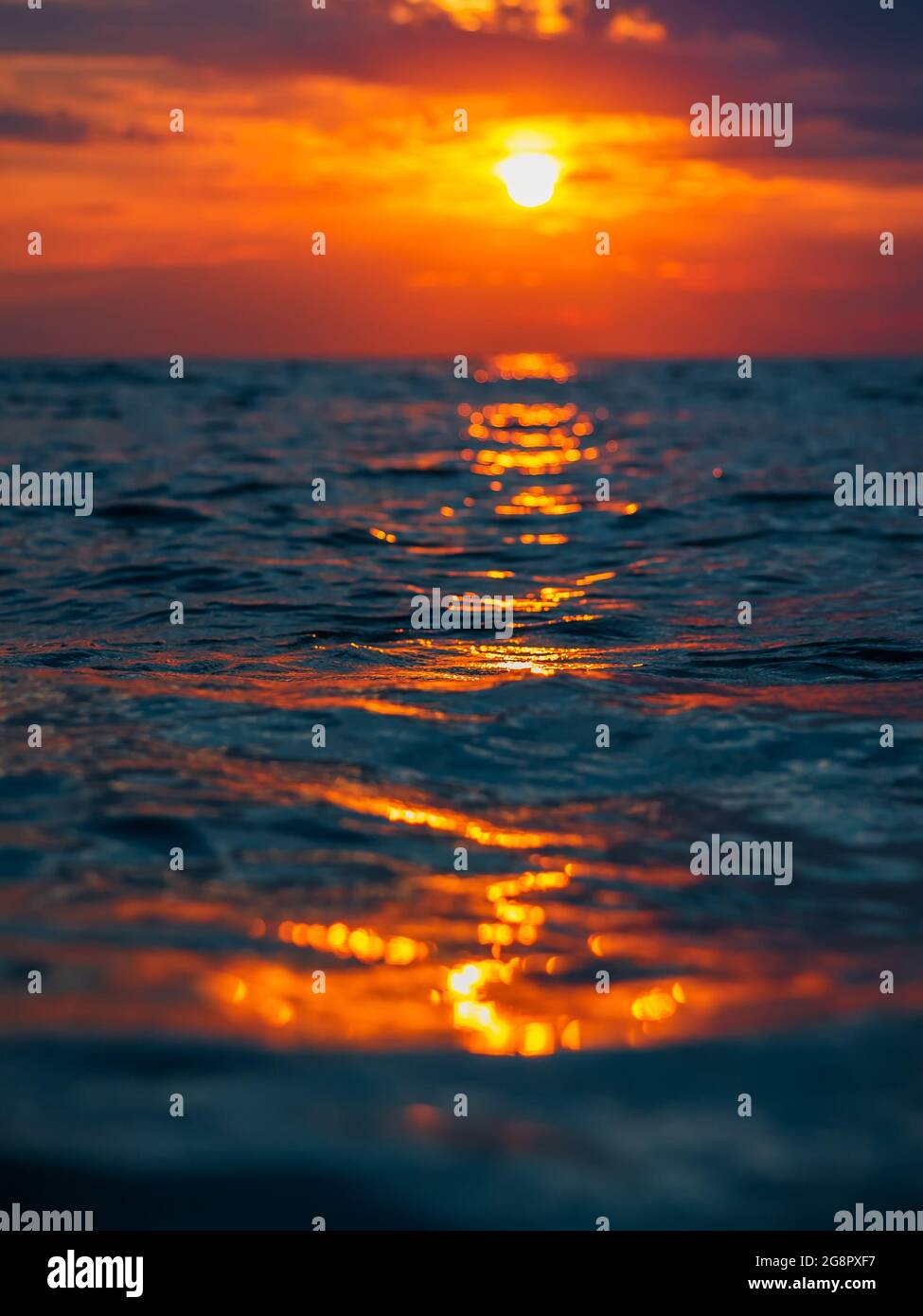 Sunset with clouds, warm colors and waves in ocean. Stock Photo