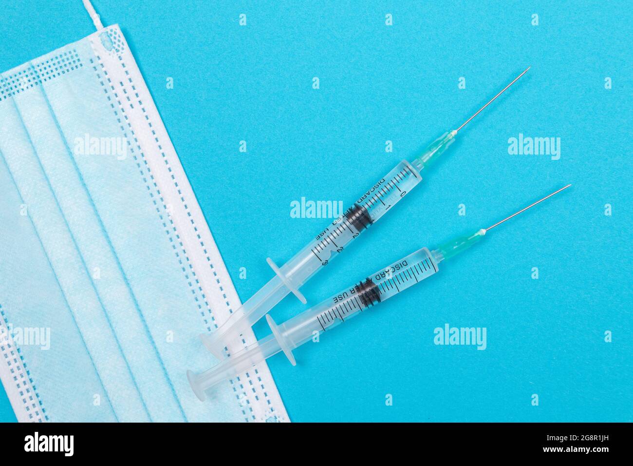 Several Syringe and Face Mask on Blue Table - Top View. Syringes are Prepared for Vaccination or Injection. Medical Experiment. Blue Disposable Medical Mask. Virus protection - Flat Lay Stock Photo