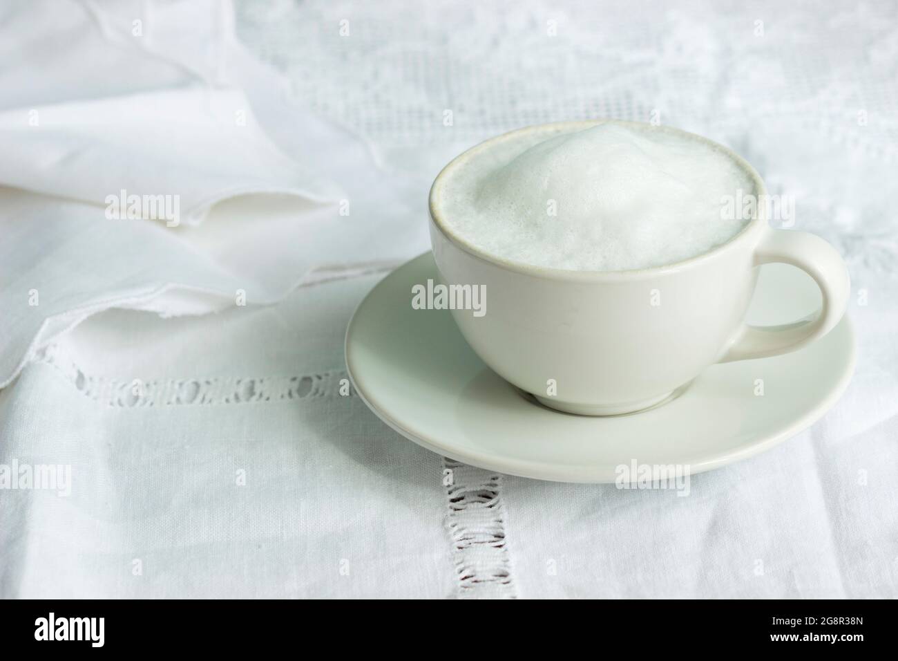 Cappuccino in a light cup on a vintage tablecloth. Stock Photo