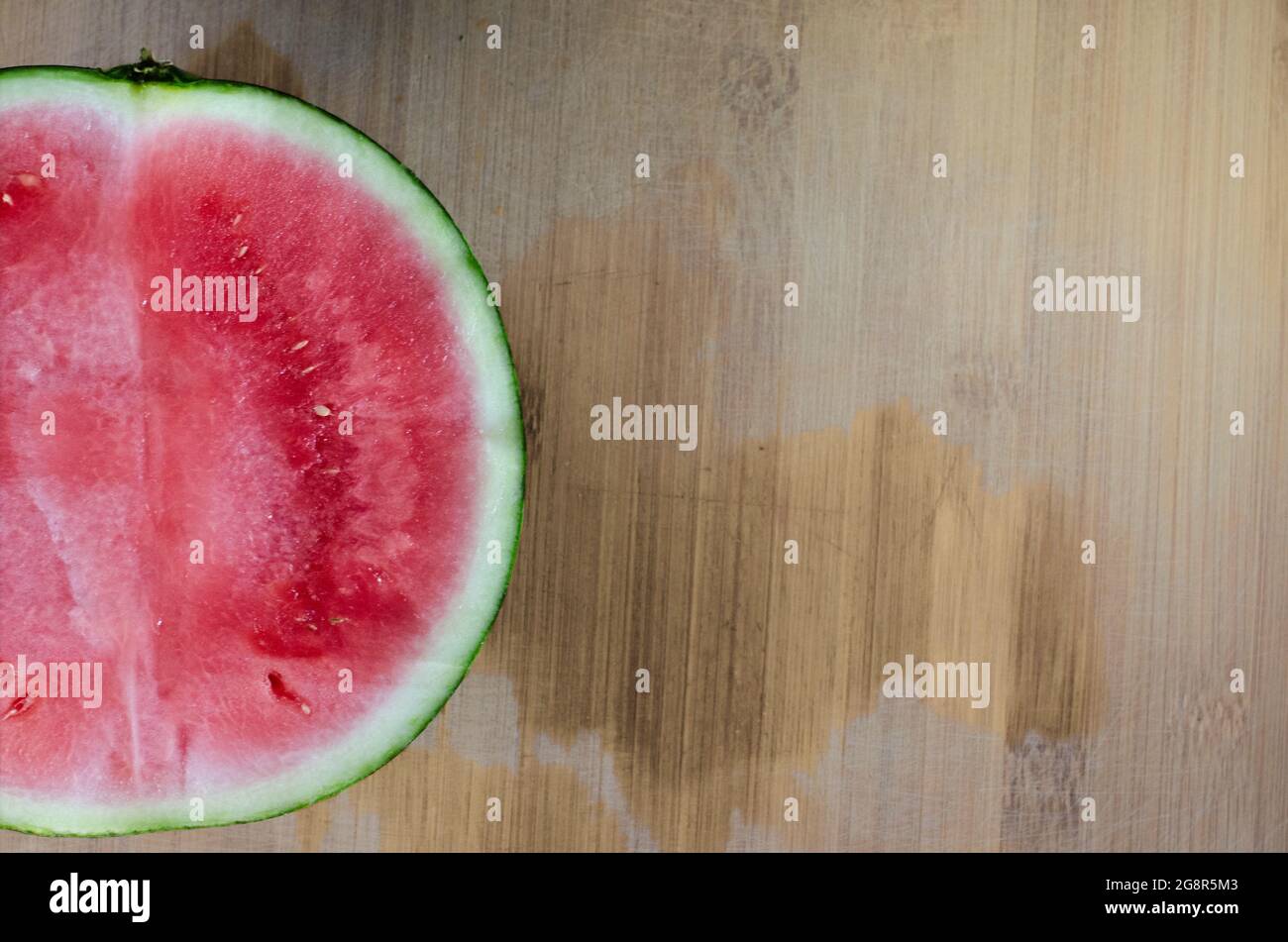 half of a watermelon in one corner and a wooden table at the bottom. Stock Photo