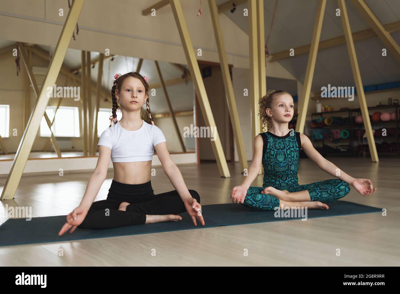 Two little girls practicing yoga are engaged in meditation sitting in the lotus position in the studio Stock Photo
