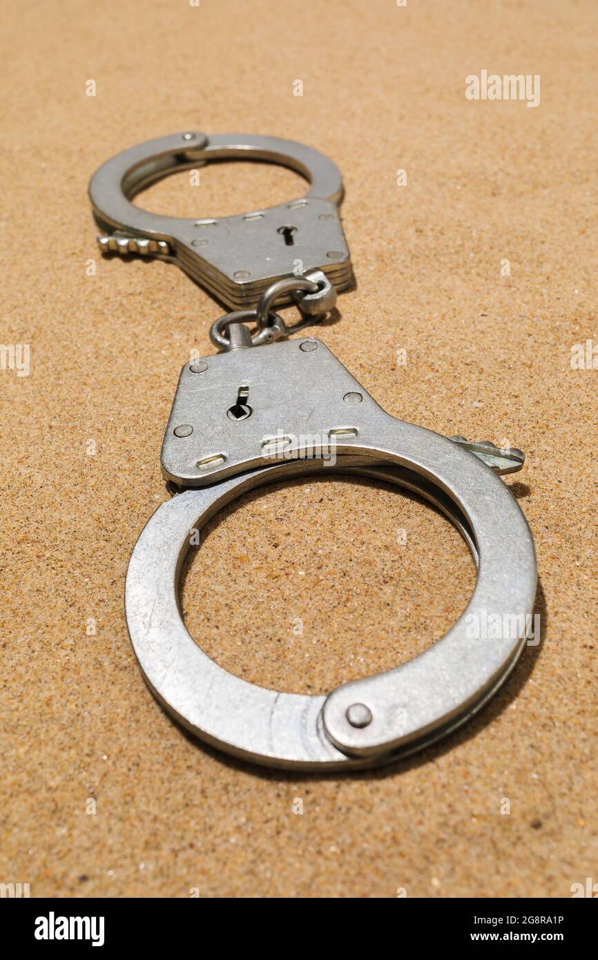 Closed silver handcuffs on the sand, close-up Stock Photo