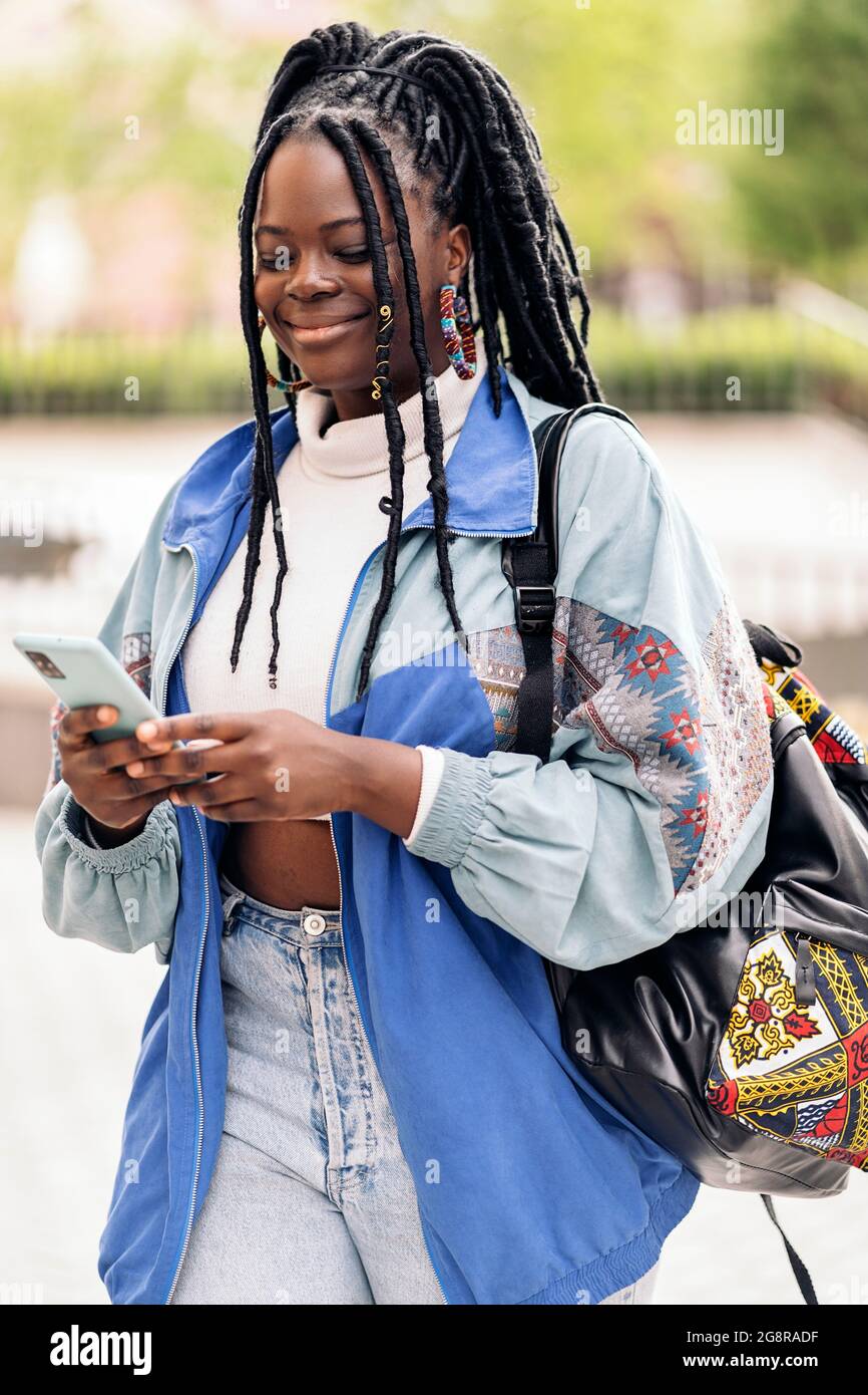 Happy african woman with cool braids walking in the street and typing ...