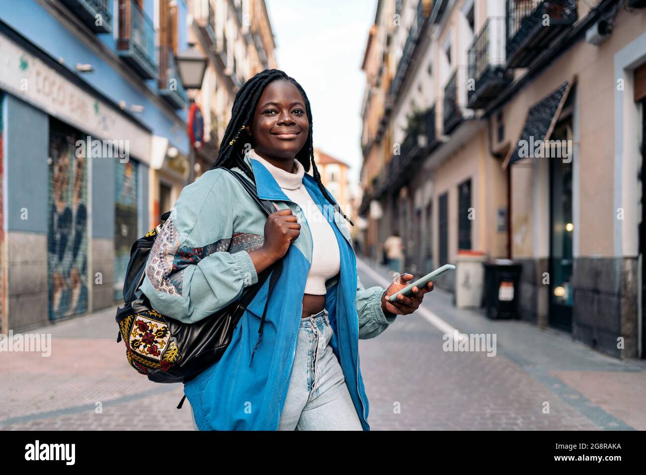 Happy african woman with cool braids walking in the street and using ...