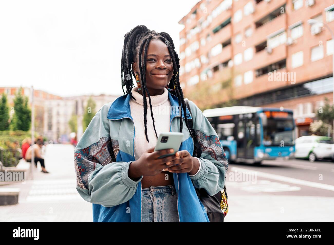 Happy african woman with cool braids walking in the street and typing ...