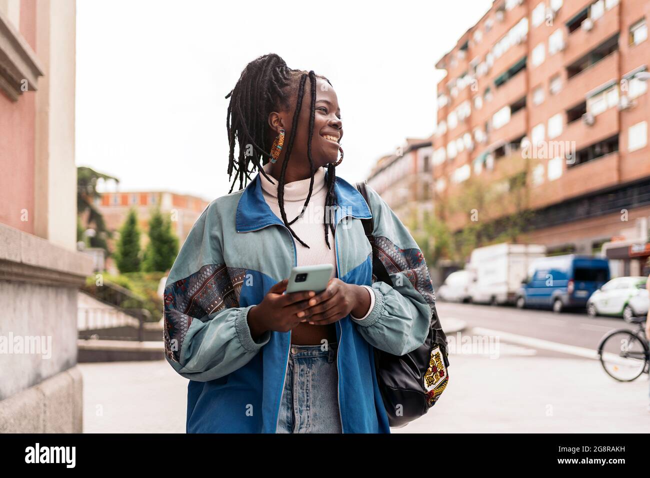 Happy african woman with cool braids walking in the street and typing ...