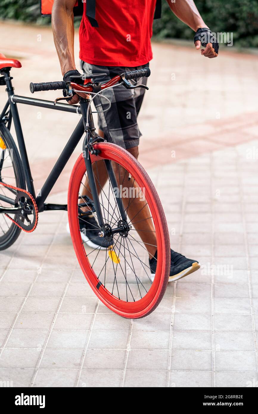 Unrecognized african delivery man walking in the city with his cool bike. Stock Photo