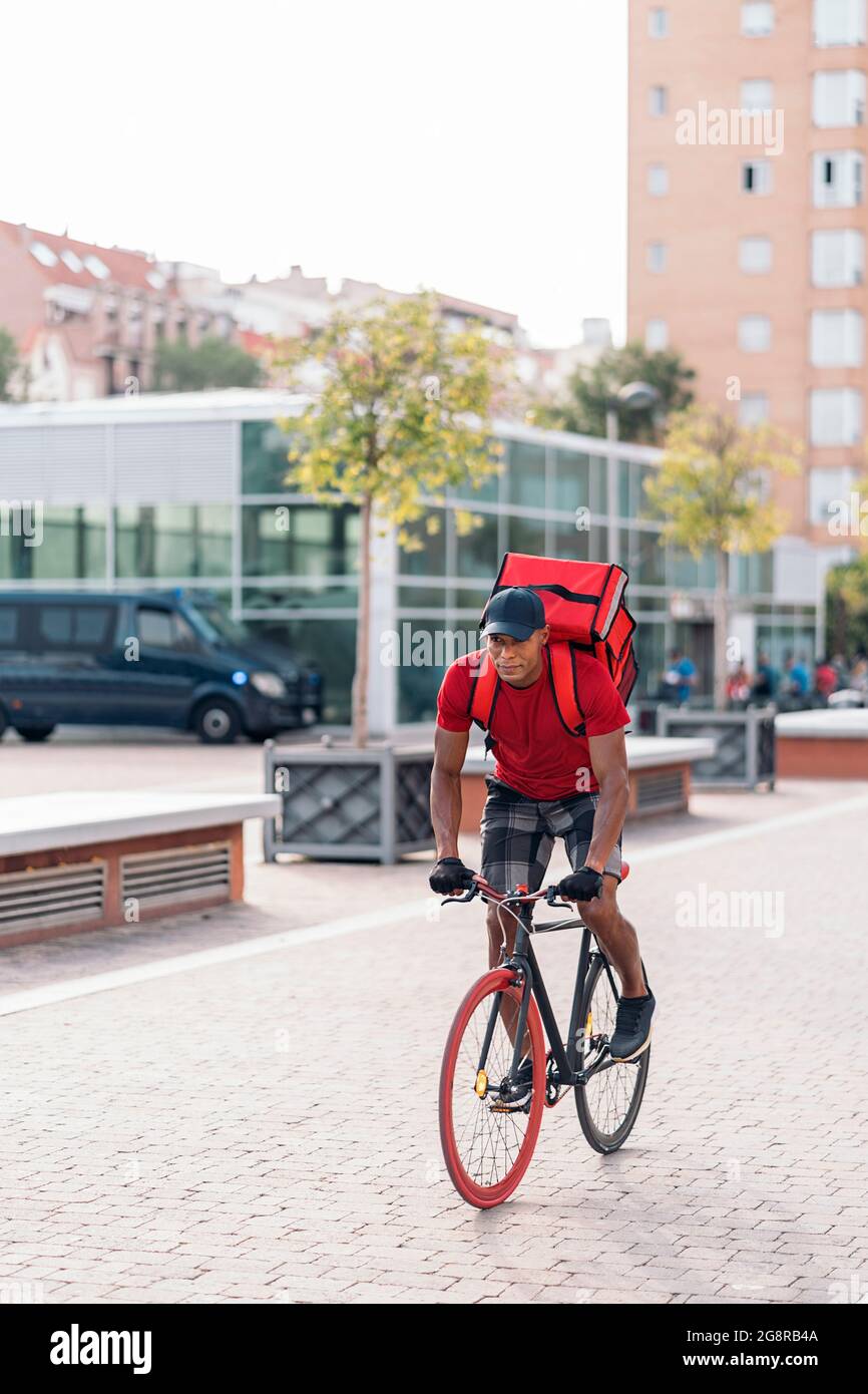 Strong african american delivery man riding his bike and carrying a package in the city. Stock Photo