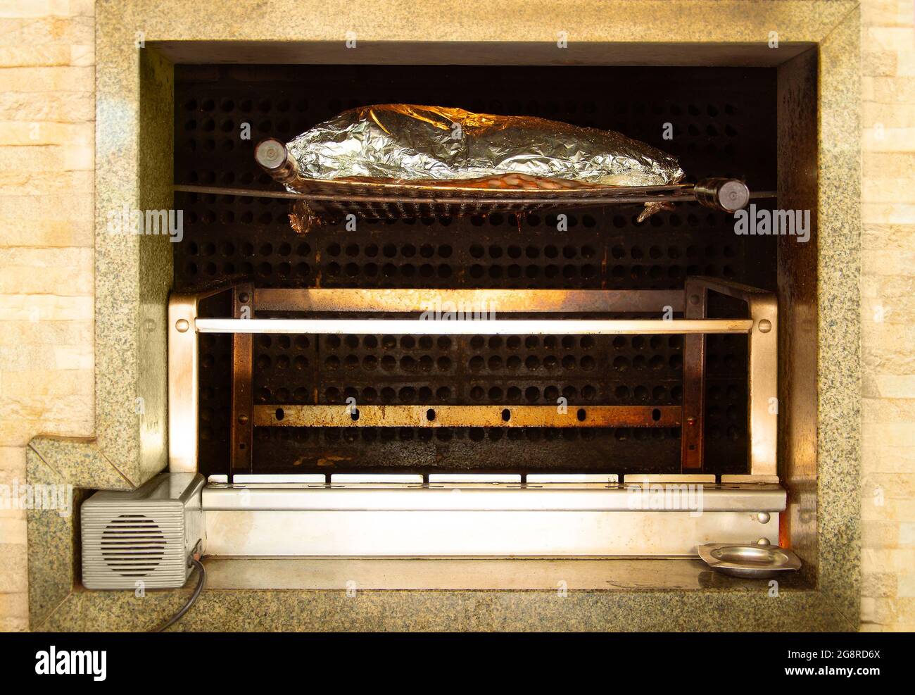 Large piece of rib wrapped in tin foil, slowly roasting on the wood