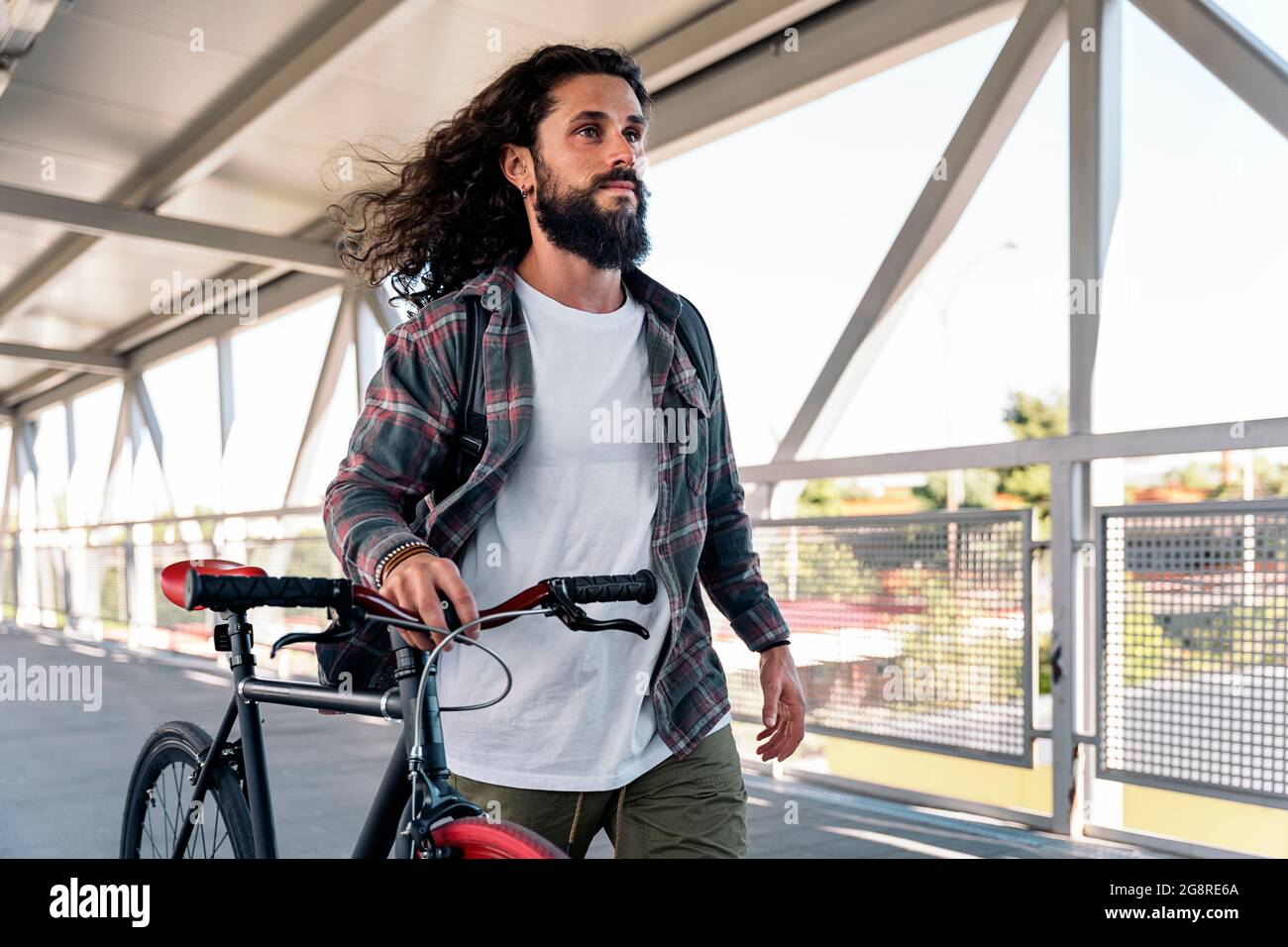 Cool bearded man with long hair smiling and looking at front while holding  his bike Stock Photo - Alamy