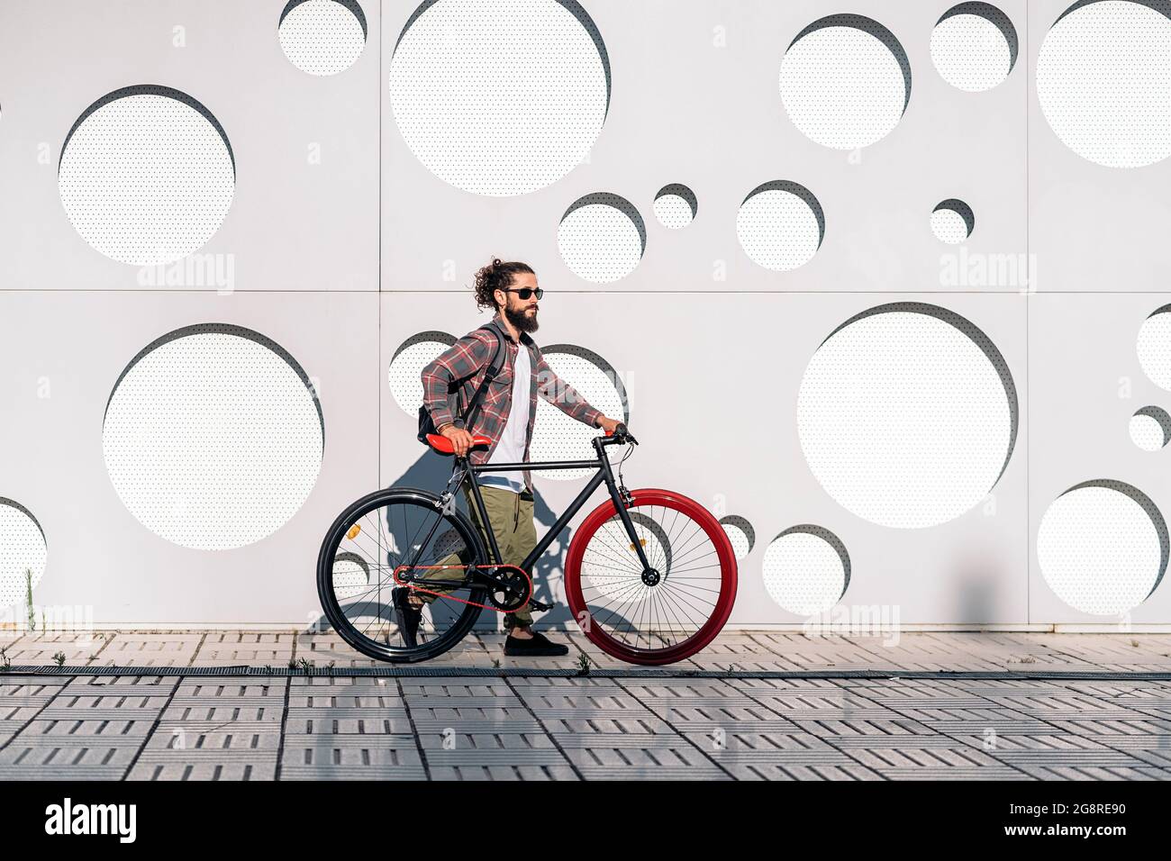 Confident man with long beard walking in the street with his cool bike. Stock Photo