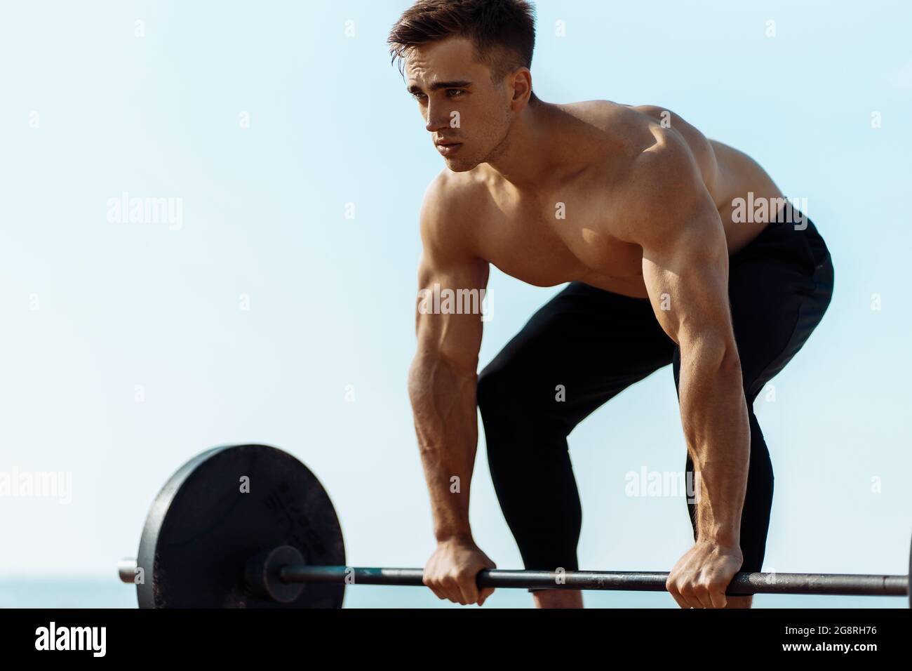Young muscular man doing chest workout with dumbbells with large weights, on the beach in the open air, Handsome man with big muscles, posing Stock Photo