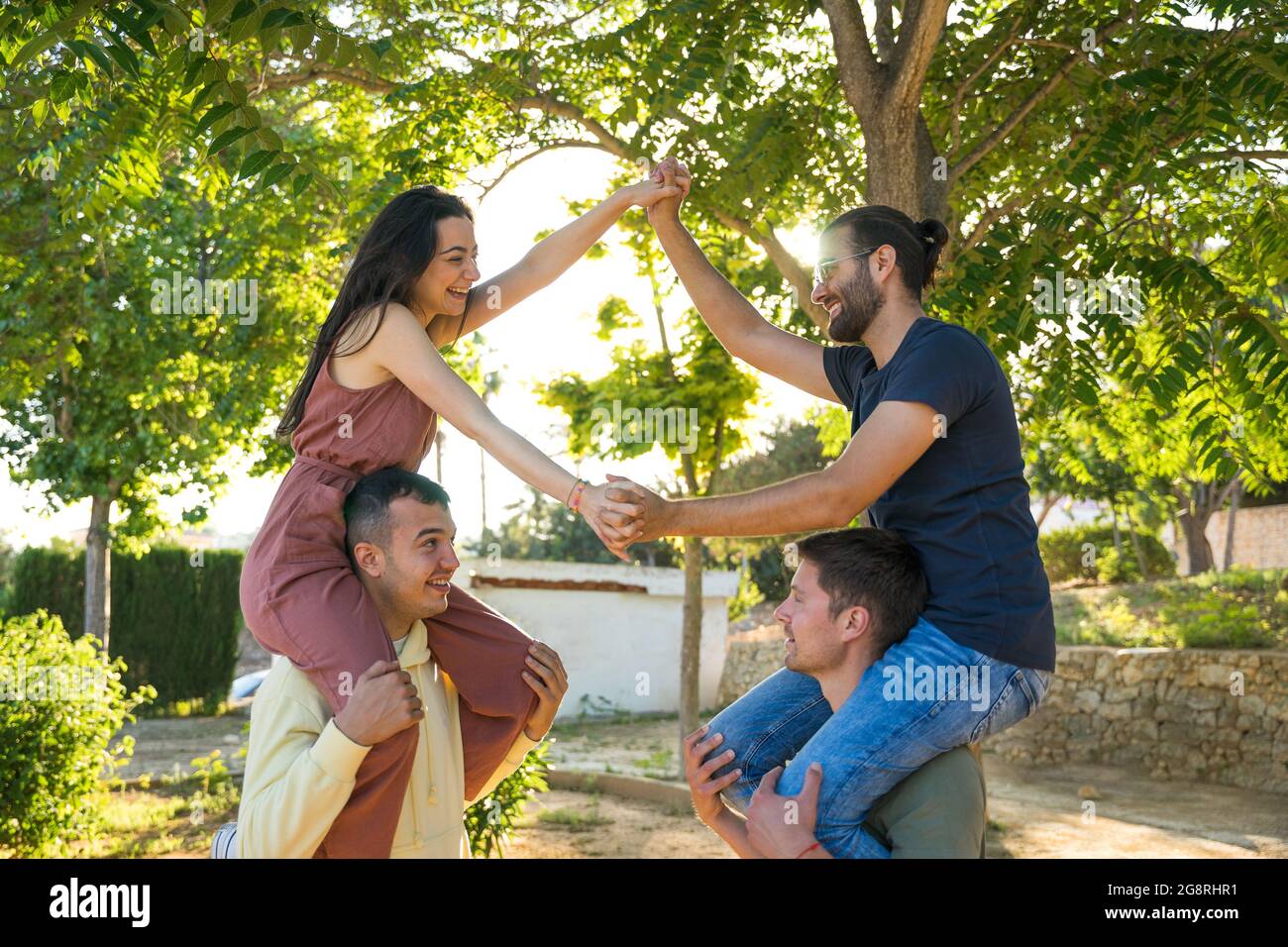 Happy friends in the park. They are on the shoulders. They are wearing colourful clothes. They are laughing and looking at each other. They are holdin Stock Photo