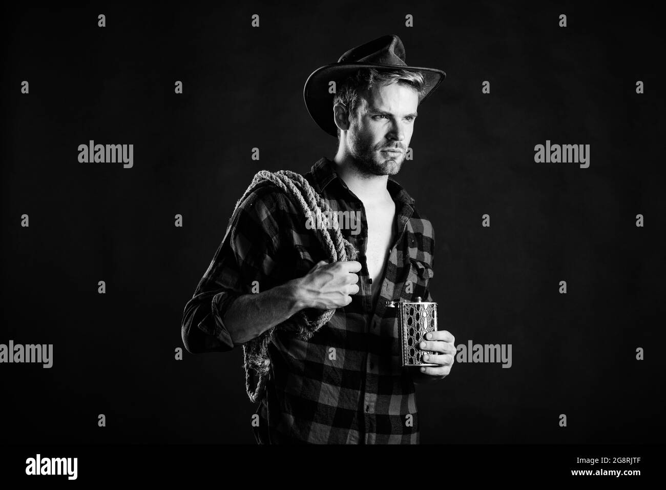 Sheriff concept. Brutal cowboy drinking alcohol. Western culture. Man wearing hat hold rope and flask. Lasso tool of American cowboy. Man handsome Stock Photo