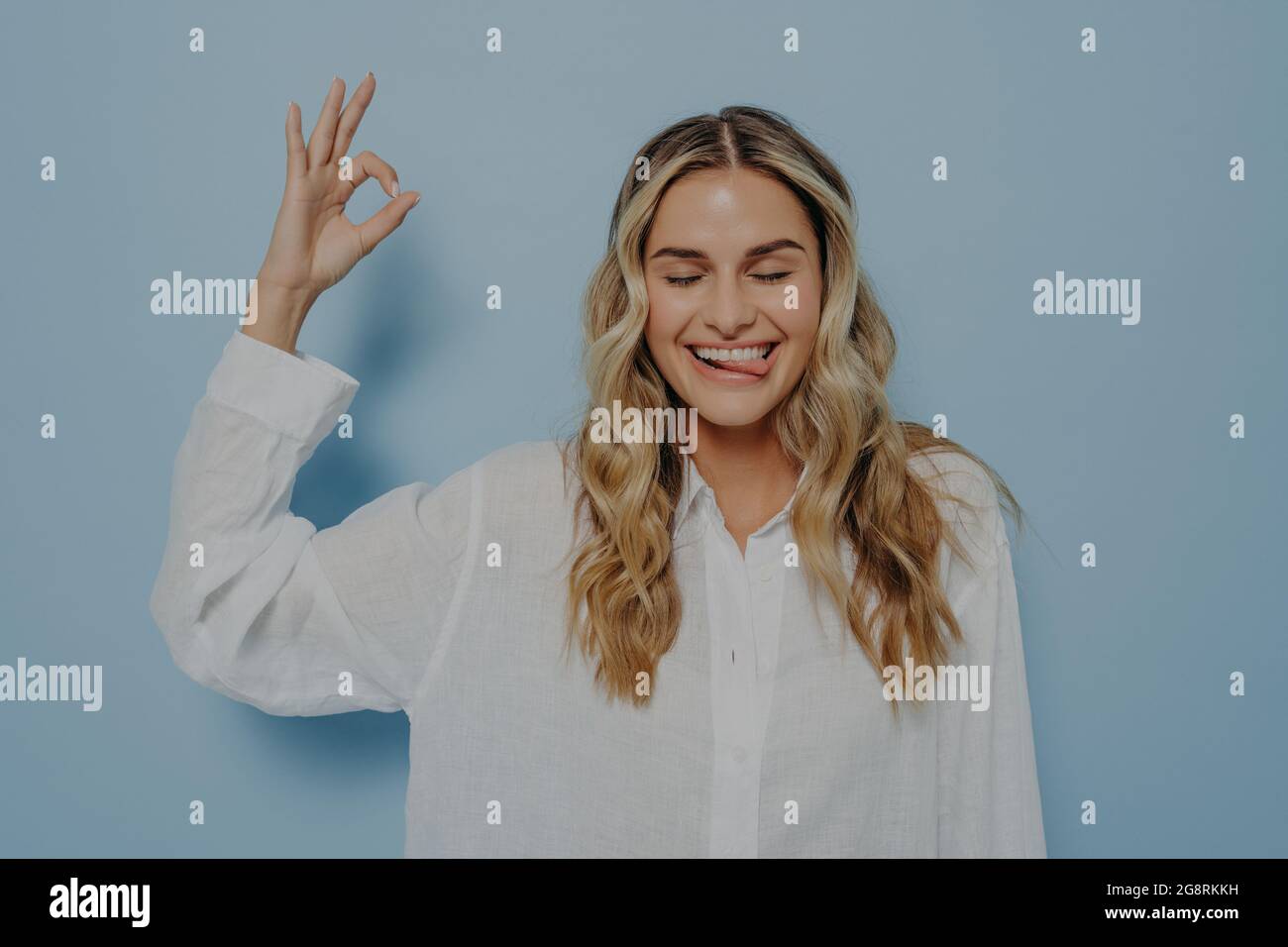 Crazy blonde woman making ok gesture while showing tongue Stock Photo