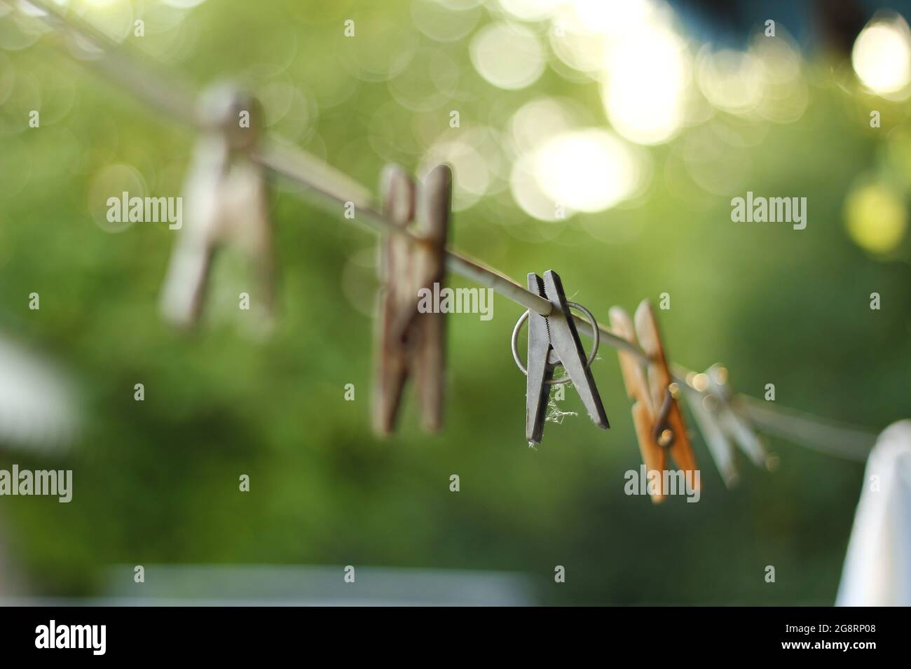 Different clothespins hang on a rope in the sun with soft bokeh. Stock Photo