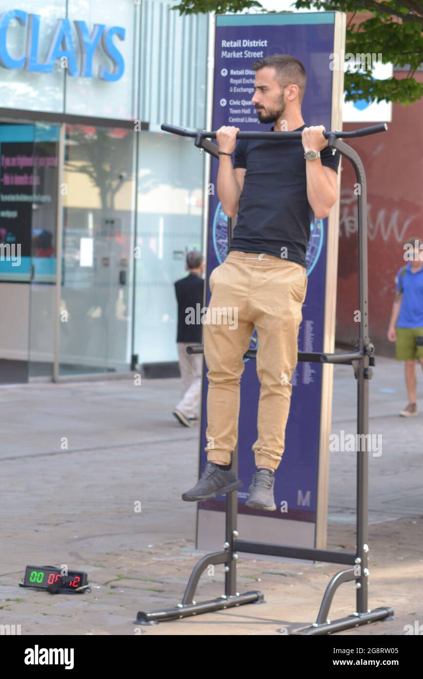 Men accept a challenge to keep themselves off the ground for two minutes at a pull-up and dip station or pull up rack for gravity fitness and weight training on Market Street, Manchester, UK. None pictured succeeded. On offer was £5 if they could do it and the offer of an audition for a film as strong men. Stock Photo