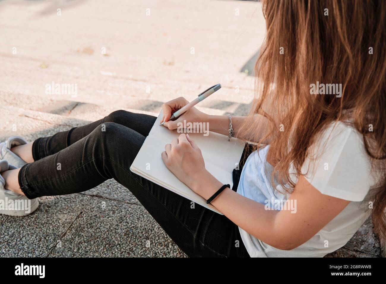 Unrecognizable woman sitting on stairs on a sunny day studying outdoors. Concept of education Stock Photo